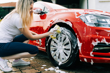 Young woman washing her car with sponge.