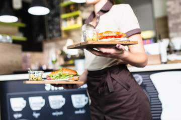 Female waitress is carrying two plates with sandwiches. - obrazy, fototapety, plakaty