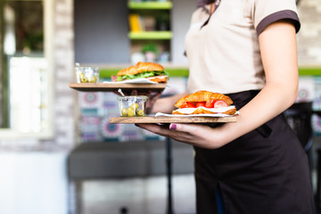 Female waitress is carrying two plates with sandwiches. - obrazy, fototapety, plakaty