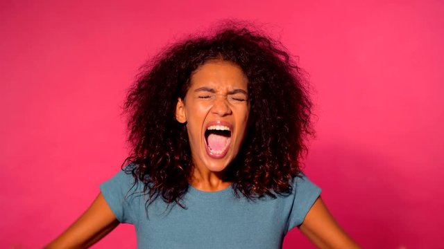 Close up of young african american stressed afro girl shouting isolated over pink background. Slow motion. Stressed and depressed woman in green clothing. 4k