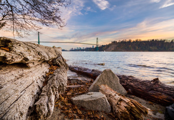 Log on the beach with the Lions Gate Bridge in the background at sunset.