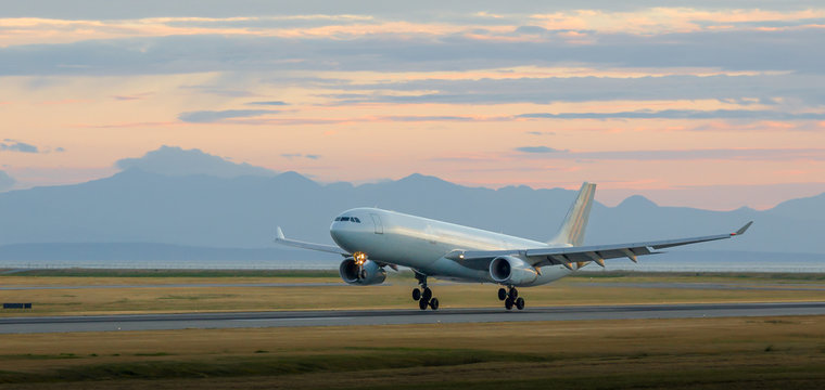 Aircraft landing at YVR at dusk with mountains in the background.