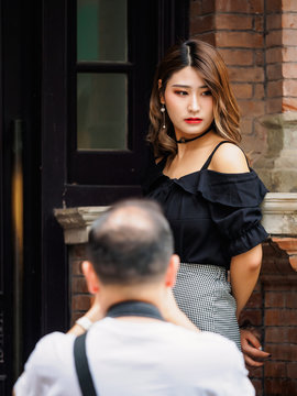 Rear view of an unrecognizable middle aged photographer taking photos for a pretty young lady in black dress in street.
