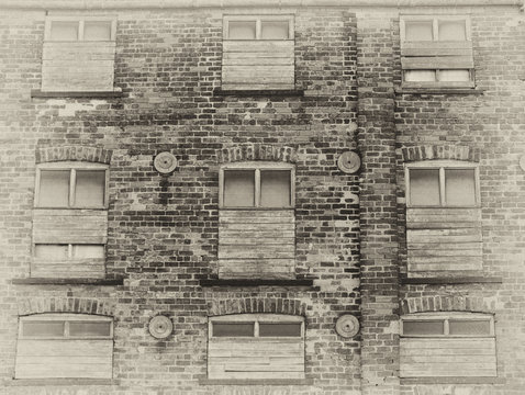 sepia view of an old abandoned commercial warehouse building with weathered brick walls and boarded up windows
