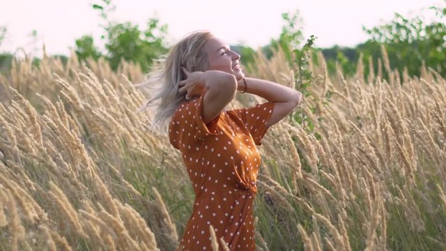 attractive fun hippie blonde woman in the field at sunset having good time outdoors. Slow motion. Female spinning in the field
