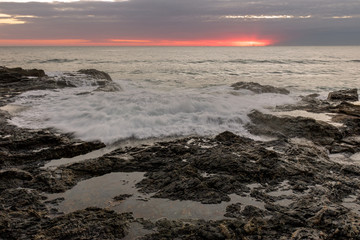 waves running onto the rock with a pink sky