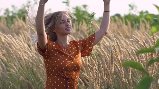 attractive fun hippie blonde woman in the field at sunset having good time outdoors. Slow motion. Female spinning in the field