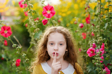 Little girl keeps fore finger on lips asks for silence.