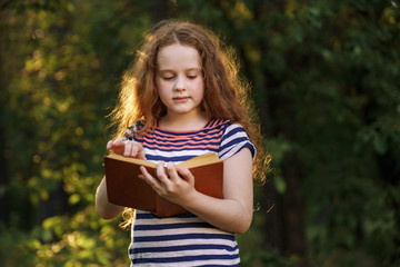 Smart little girl reading the book outdoors.
