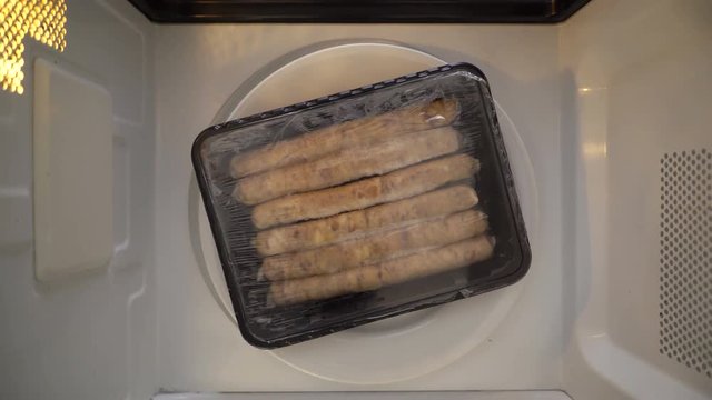 Top view defrosting sausages in microwave. Plastic container with breakfast sausage spinning in microwave.