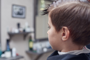 Caucasian boy getting hairstyle by hairdresser in barbershop.