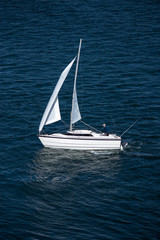 Solo sailor in small sailboat on blue water with reflection of white sails