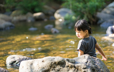little asian girl playing in waterfall stream with water splash