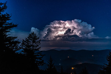 A huge thunderstorm with active lightning lighting up the clouds is seen from the high peak of...