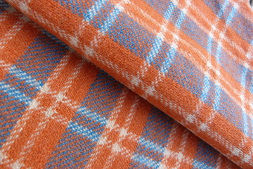 woolen fabric in a cage close-up gray orange stripes squares drape nap vintage coat plaid background for decor rolls cloth folds on fabric natural material