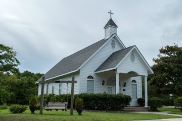 White country church with wooden siding and cross on the cupola