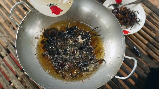Woman pouring fried oil into a wok with deep-frying tarantulas 