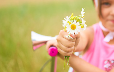 Little smiling girl in a protective helmet on a bicycle picked up flowers in a summer field and...