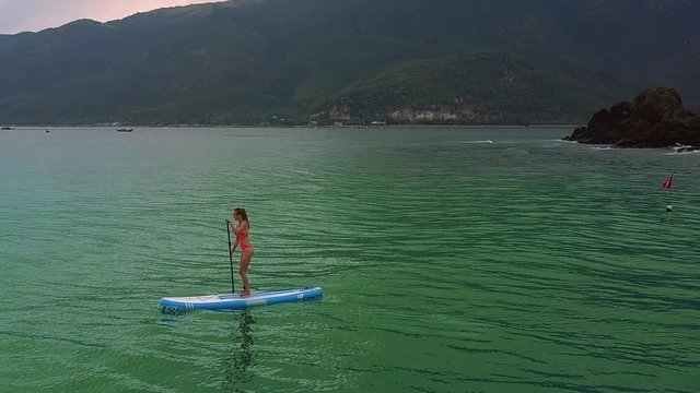 girl in red bikini on paddleboard against hilly coast