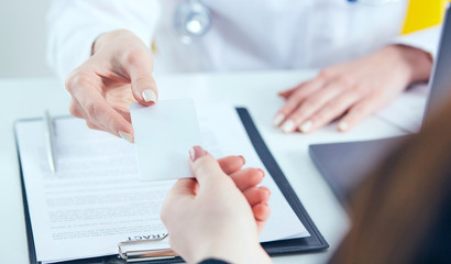 Female physician hand give white blank calling card to businesswoman closeup in office.