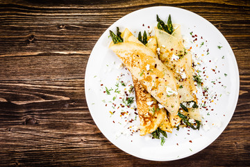 Crepes with spinach and cottage cheese on wooden background 