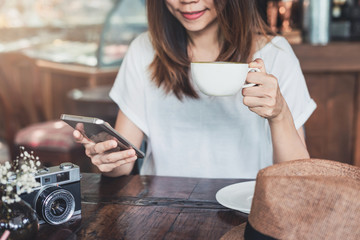 Young woman using smart phone and drinking coffee in cafe