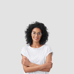 Vertical shot of happy dark skinned female with curly hair, glad to be promoted at work, wears...