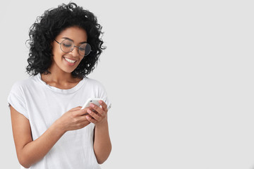 Cheerful African American with crisp hair, holds modern smart phone, happy to recieve message,...