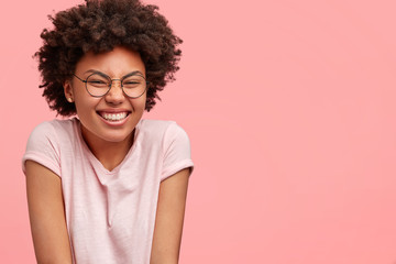Cheerful dark skinned female student giggles at camera, hears jokes from groupmates, shruggs...
