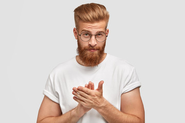 Confident handsome male applauds as greets someone, has thick ginger beard and trendy haircut,...