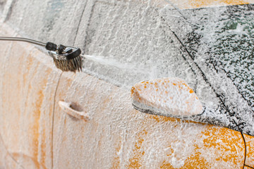 Yellow car being washed in self serve carwash. Shampoo and foam spraying to the side mirror and window.
