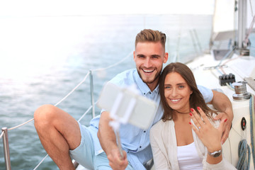 Happy couple taking a selfie after engagement proposal at sailing boat, relaxing on a yacht at the...