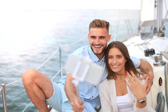 Happy couple taking a selfie after engagement proposal at sailing boat, relaxing on a yacht at the sea.
