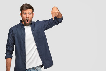 Horizontal shot of amazed man with stupefied expression, points down with index finger, dressed in casual clothes, shows free space for your advertising content. Astonished young Caucasian man © WHstudio Leushin N