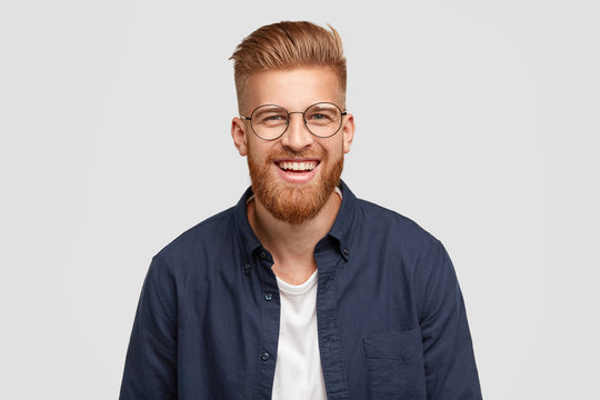 Pleased cheerful redhaired male with pleasant smile, giggles joyfully, spends free time with girlfriend, being in high spirit, shows white teeth, happy to have romantic relationships, stands in studio