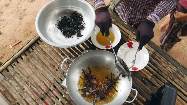 Woman taking deep fried tarantulas out of a wok and putting them in a bowl (upper view),