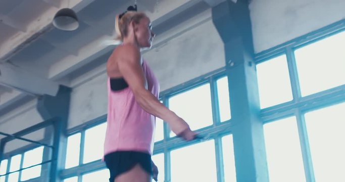 Young adult sporty Caucasian woman performing skipping rope workout in functional gym, morning shot. 4K
