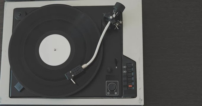The man's hand puts the needle on the vinyl record and starts the player.