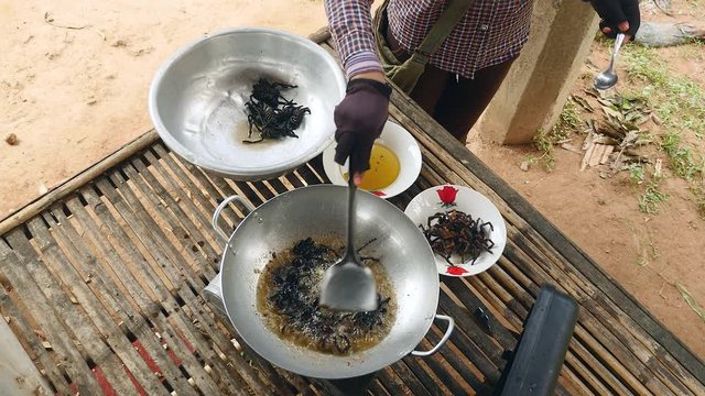 Woman turning over deep frying tarantulas inside a wok using a metal spatula (upper view)