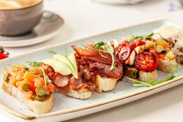 The concept of Italian cuisine, a tourist breakfast in a restaurant. different bruschetta on a long plate with a mug of coffee. Copy space, selective focus