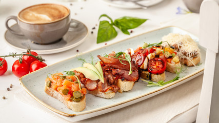 The concept of Italian cuisine, a tourist breakfast in a restaurant. different bruschetta on a long plate with a mug of coffee. Copy space, selective focus