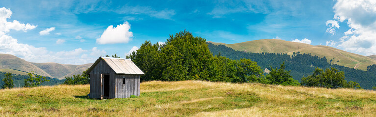wooden hut on a grassy meadow. forested mountains in the distant. beautiful panorama of summer countryside