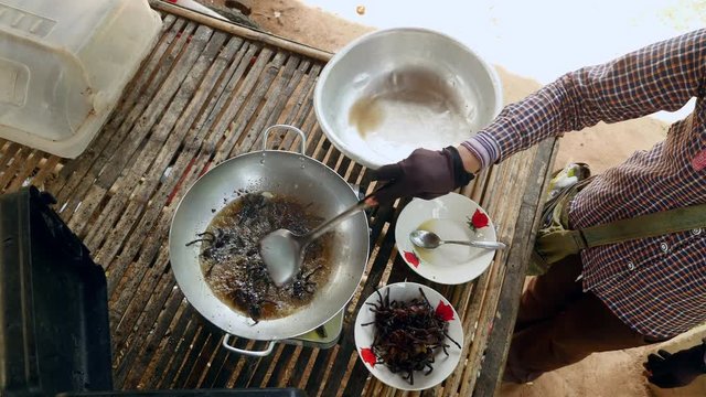 Woman turning over deep frying tarantulas inside a wok using a metal spatula (upper view)