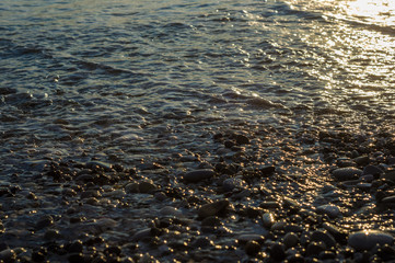 pebble stones on the sea beach, the rolling waves of the sea with foam