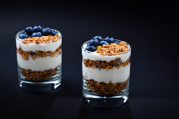 Homemade baked granola with yogurt and blueberries in a glass on a black background. Space for text or design.