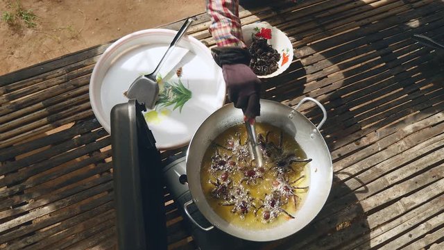 Woman turning over deep frying tarantulas inside a wok using metal tongs (upper view)