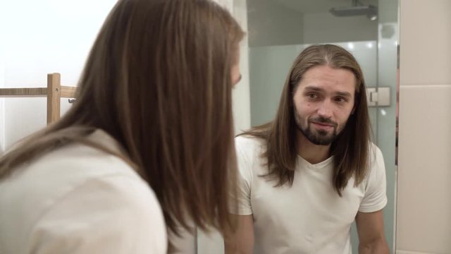 Man At Bathroom Looking In Mirror And Touching Face