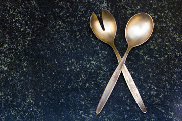 Two metallic silverware spoon and fork for salads placed on a dark marble surface, ideal for...