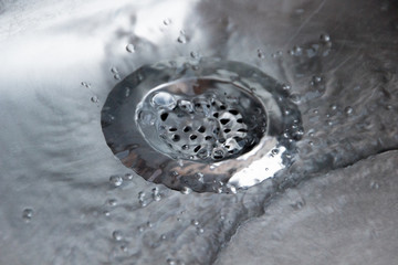 Close up of a metallic silver drain strainer in a sink with water flowing through the strainer in...
