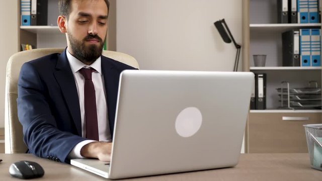 Successful hard working young antrepreneur in his office. He types on the computer keyboard then looks through some charts in a black folder